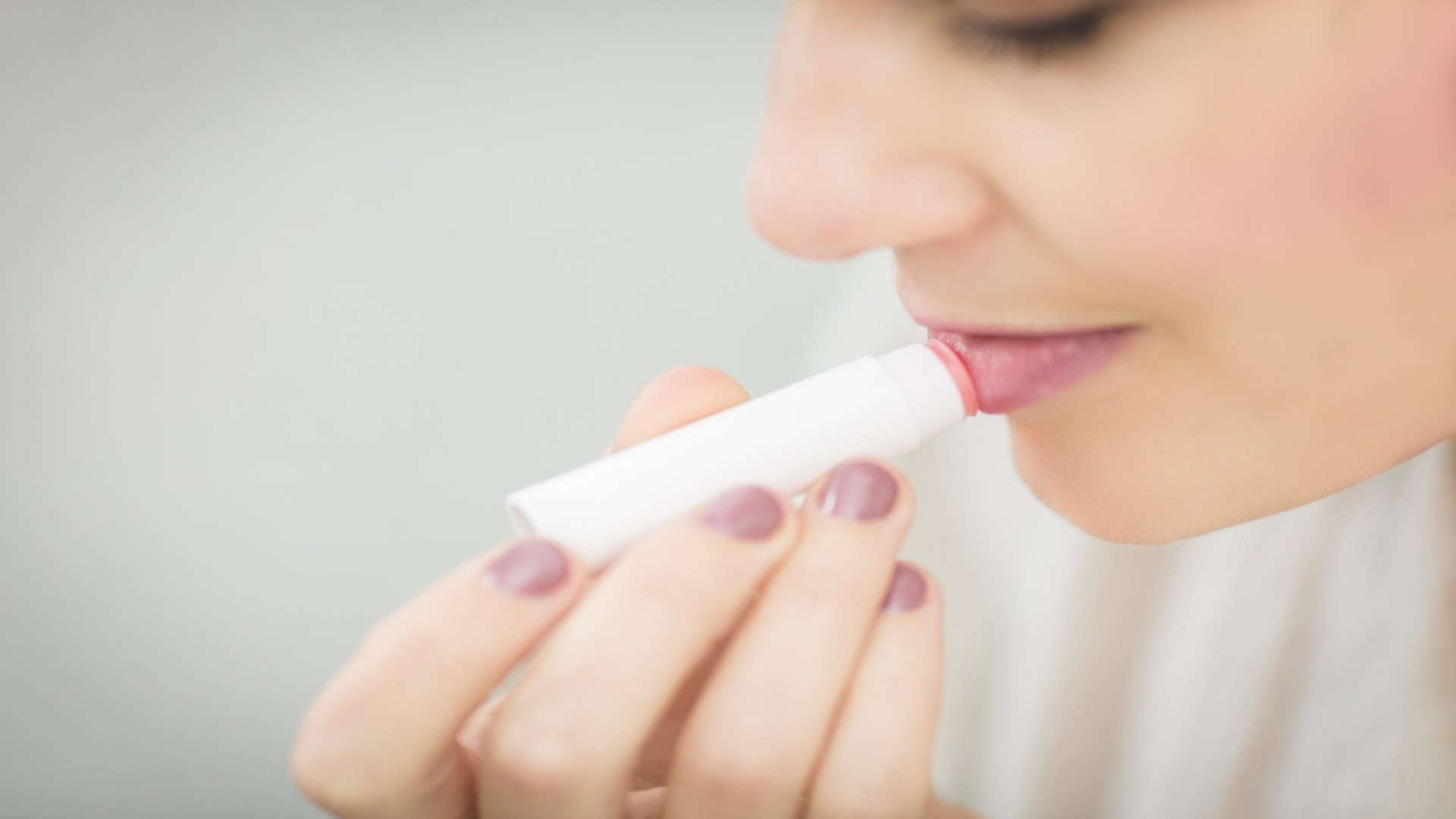 Mujer aplicándose bálsamo en los labios, cuidando su piel labial.