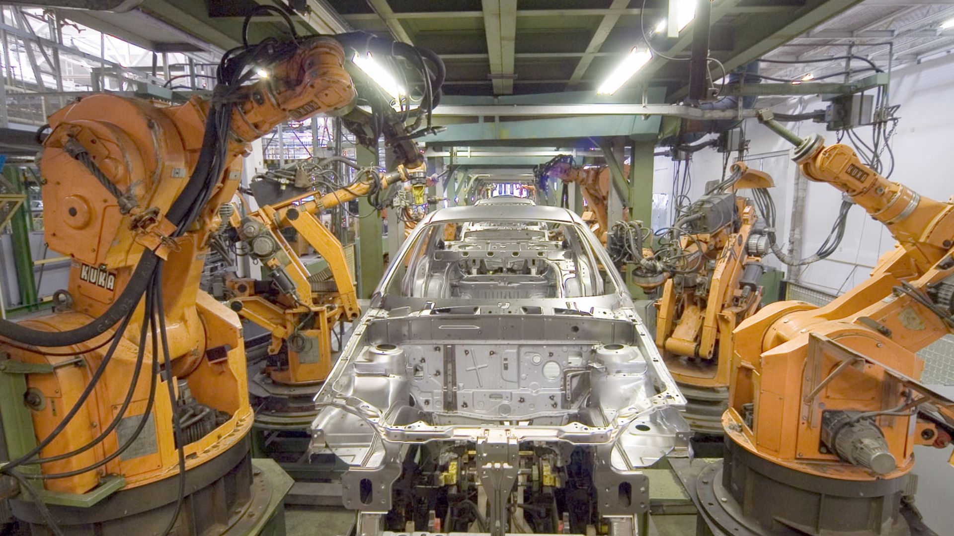 Orange industrial robots assembling a car on an automotive production line in a factory setting.